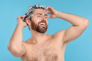 Photo of Happy man washing his hair with shampoo on light blue background