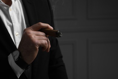 Photo of Man smoking cigar on dark grey background, closeup. Space for text