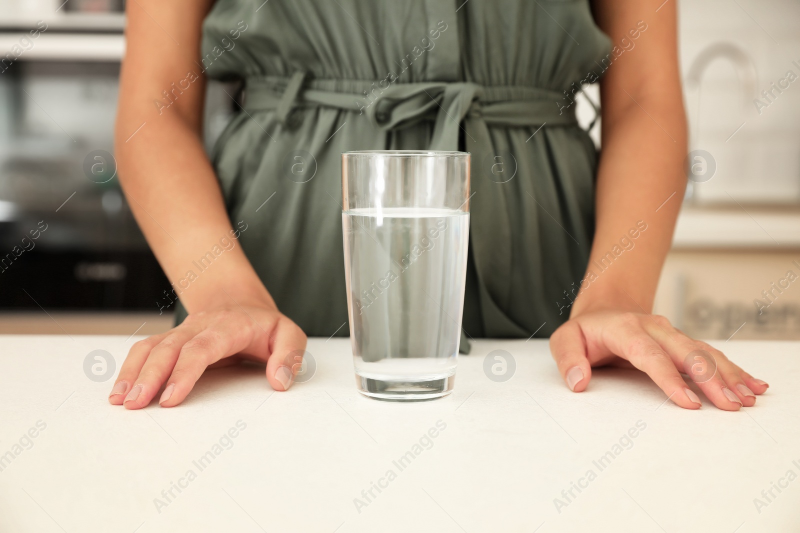 Photo of Woman with glass of water at table in kitchen, closeup