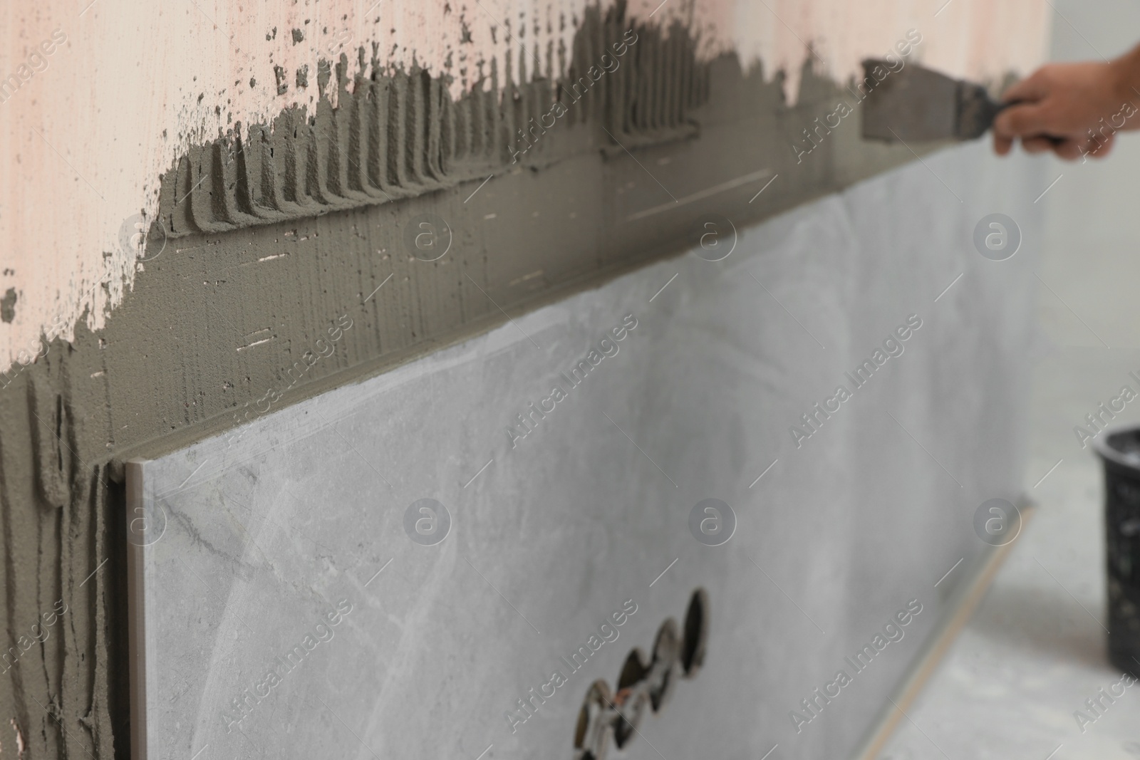 Photo of Worker spreading adhesive mix on wall, closeup. Tiles installation process