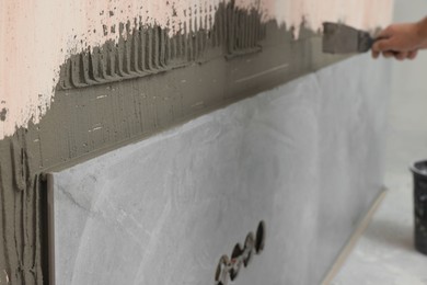 Worker spreading adhesive mix on wall, closeup. Tiles installation process