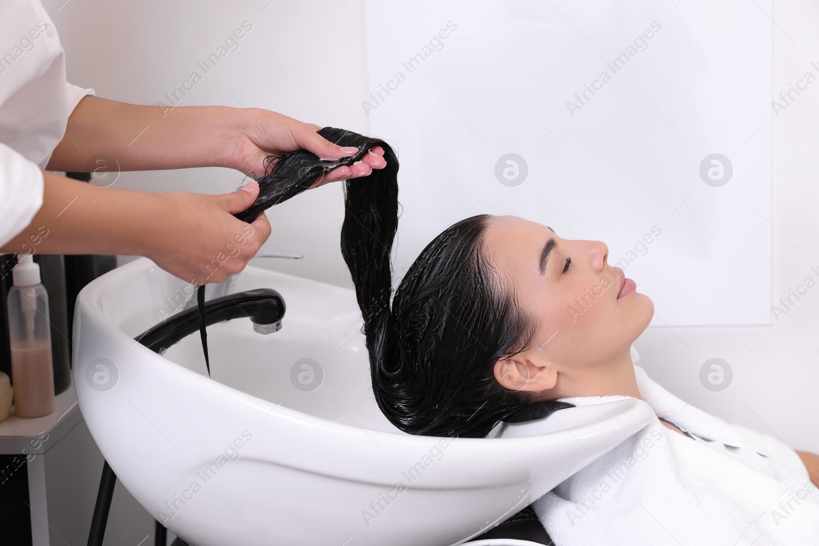 Photo of Professional hairdresser applying conditioner on woman's hair in beauty salon, closeup