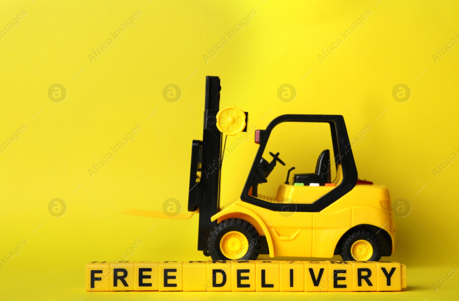 Photo of Toy forklift and cubes with words FREE DELIVERY on yellow background. Logistics and wholesale concept