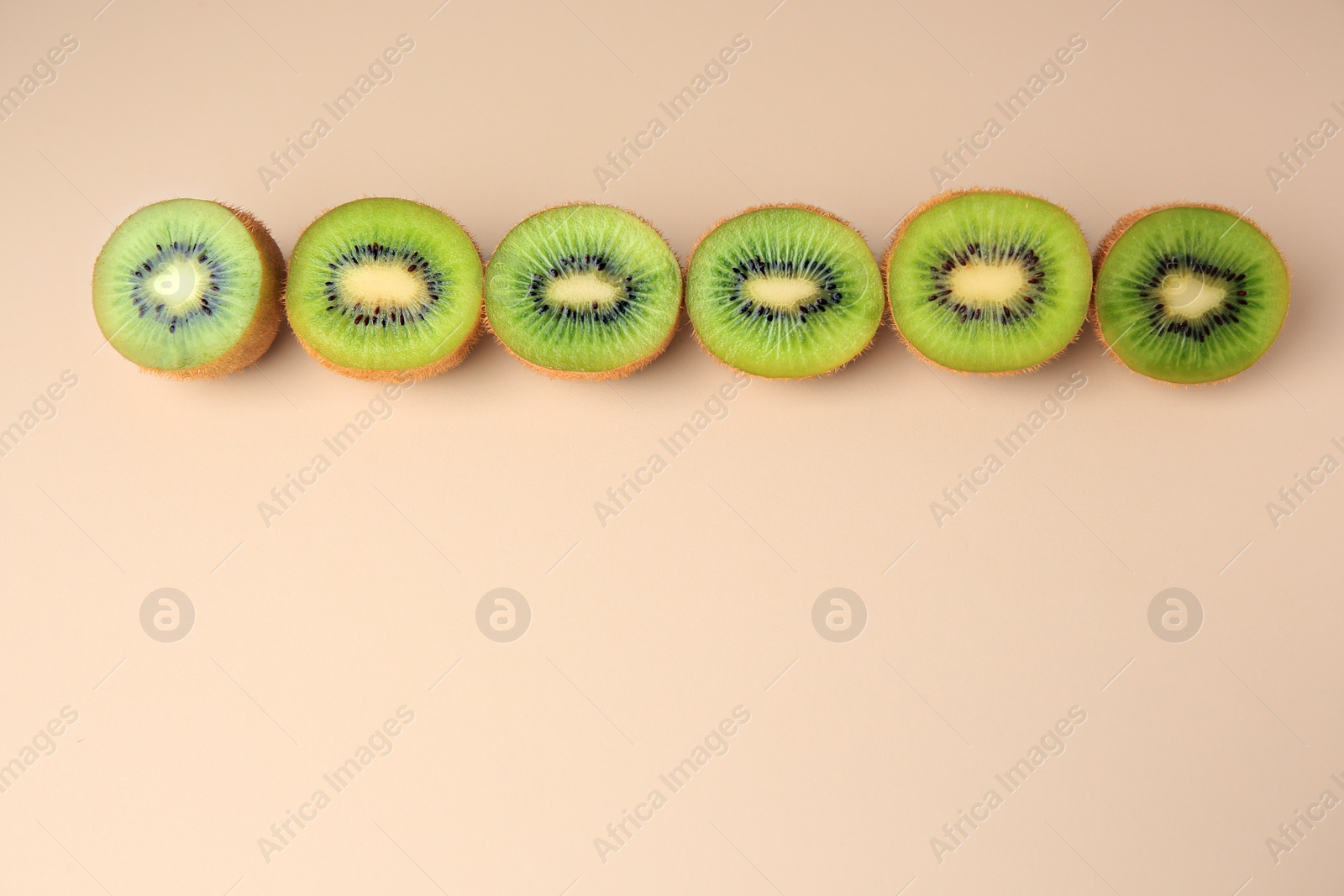 Photo of Halves of fresh kiwis on beige background, flat lay