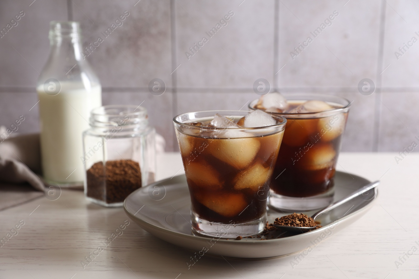 Photo of Refreshing iced coffee with milk in glasses, ingredients and spoon on light table