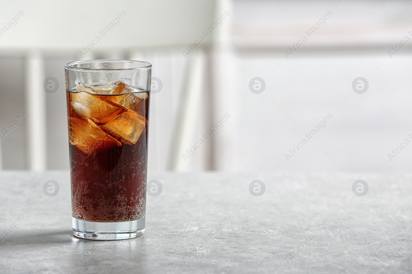 Photo of Glass of cold cola on table against blurred background. Space for text