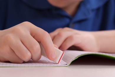 Boy erasing mistake in his notebook at white desk, closeup
