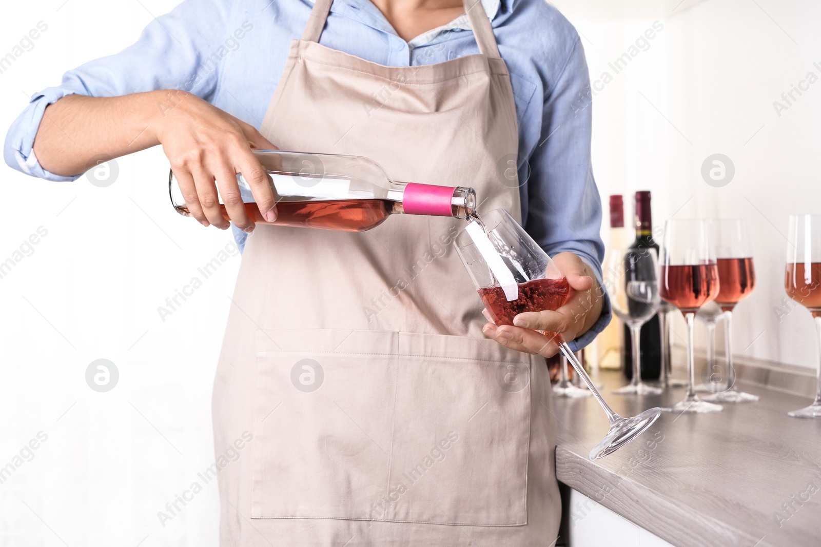 Photo of Young woman pouring delicious rose wine from bottle into glass indoors, closeup