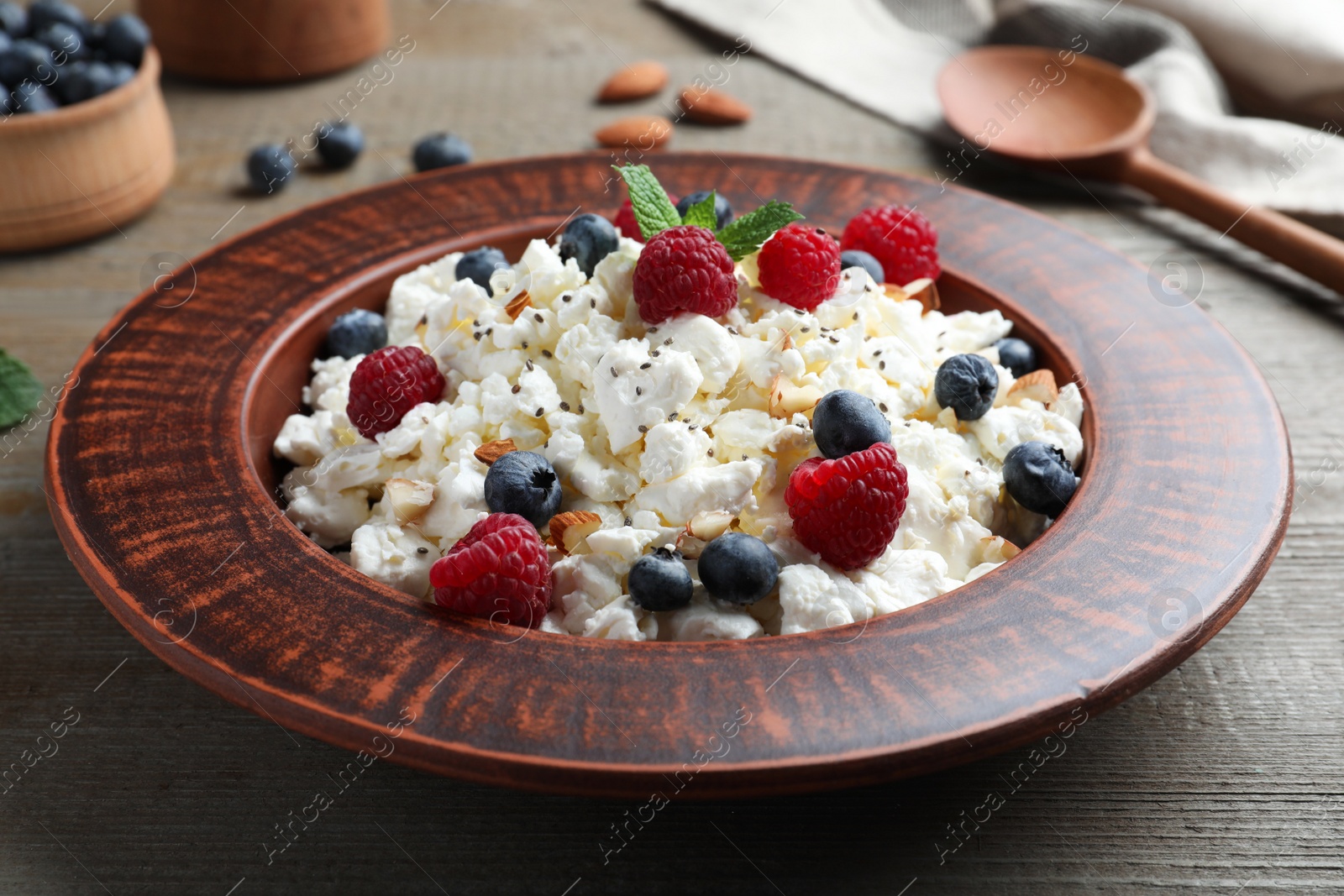 Photo of Fresh cottage cheese with berries and mint in plate on wooden table, closeup