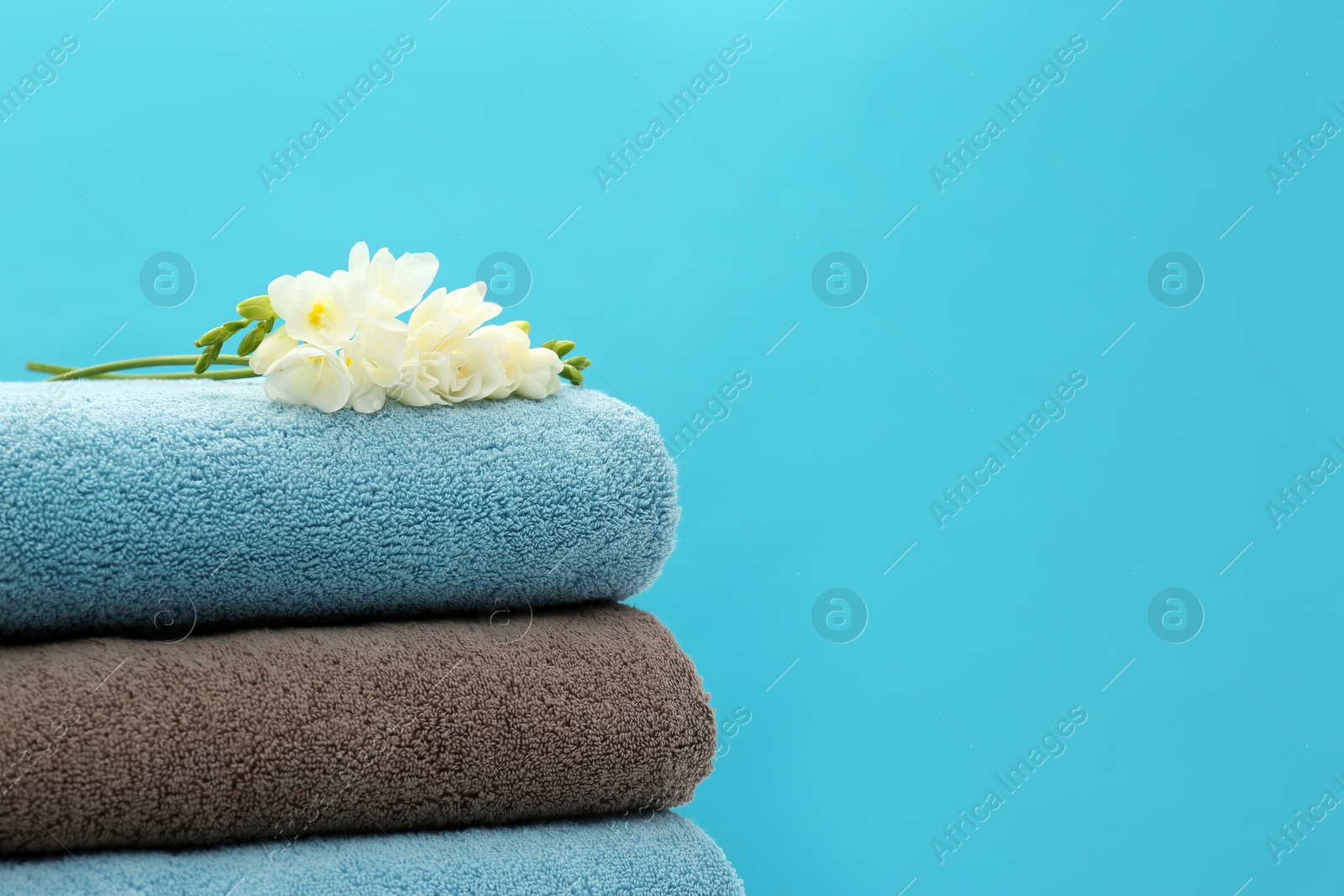 Photo of Stack of soft clean towels with beautiful flowers on color background. Space for text