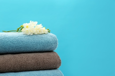 Stack of soft clean towels with beautiful flowers on color background. Space for text