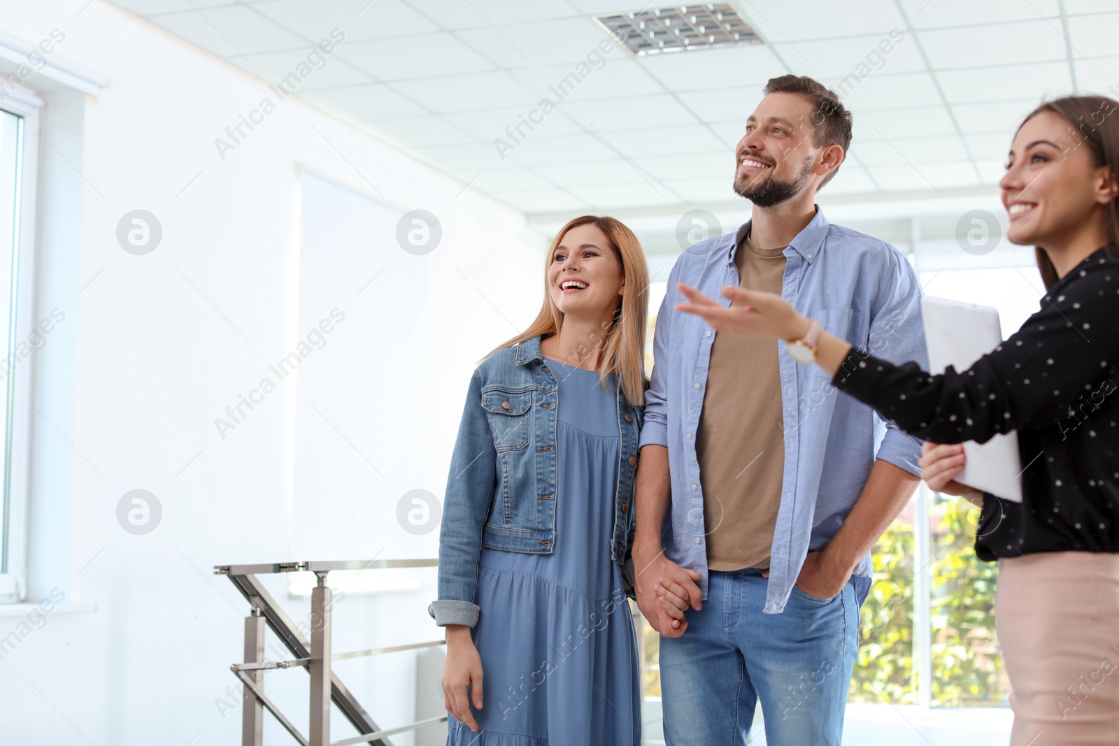 Photo of Female real estate agent showing new house to couple, indoors