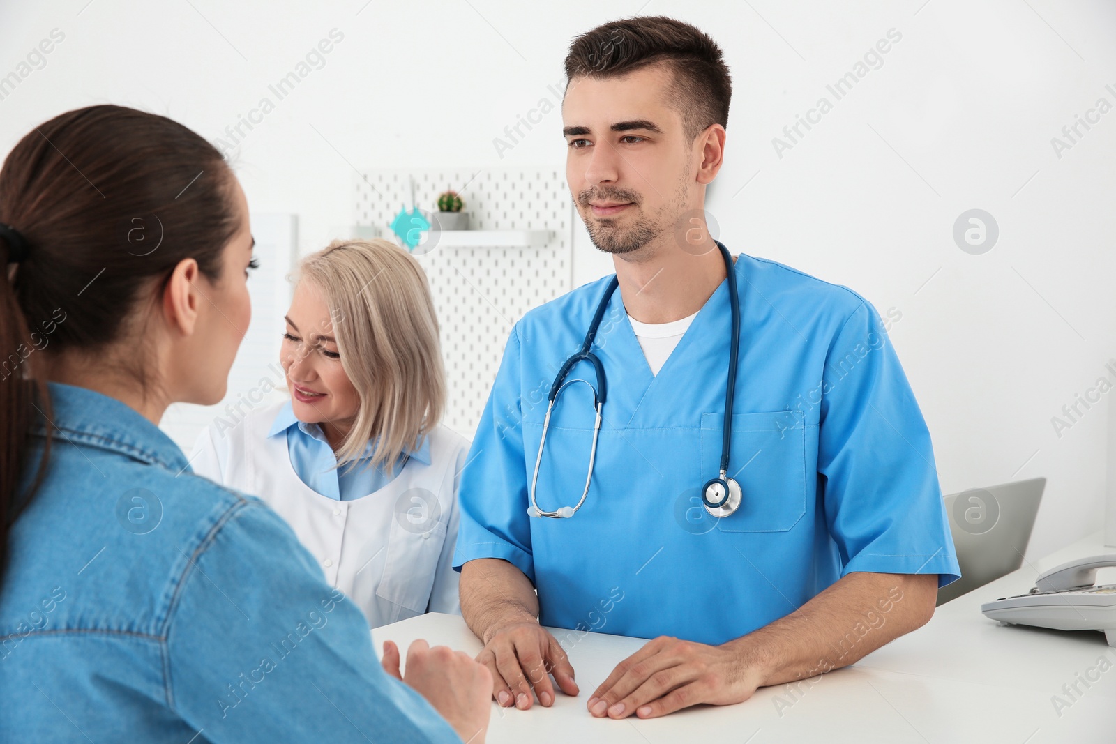 Photo of Young male doctor and senior female receptionist working with client in hospital