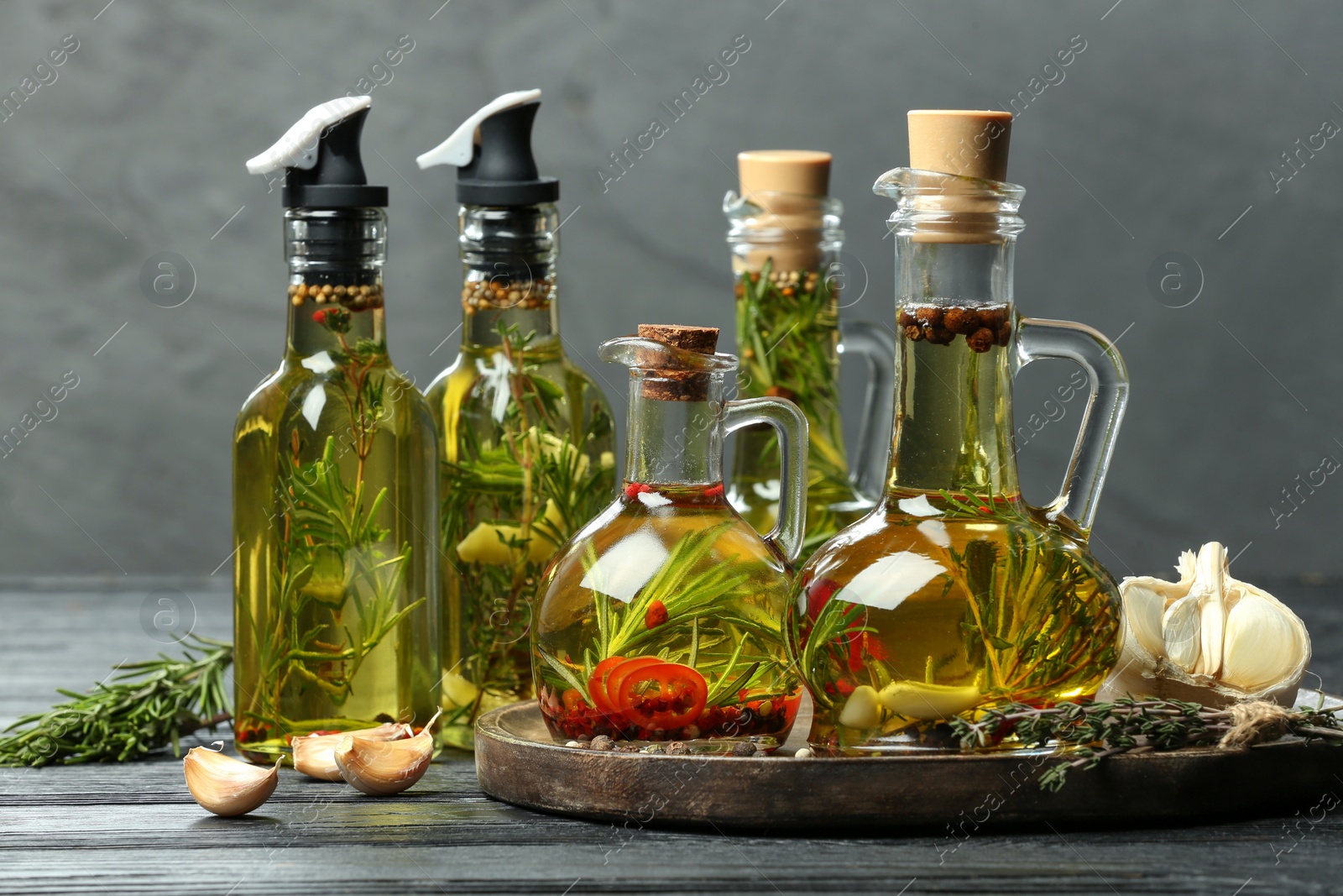 Photo of Cooking oil with different spices and herbs in bottles on grey wooden table