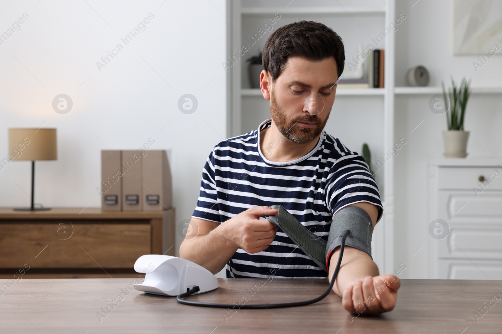 Photo of Man measuring blood pressure at wooden table in room