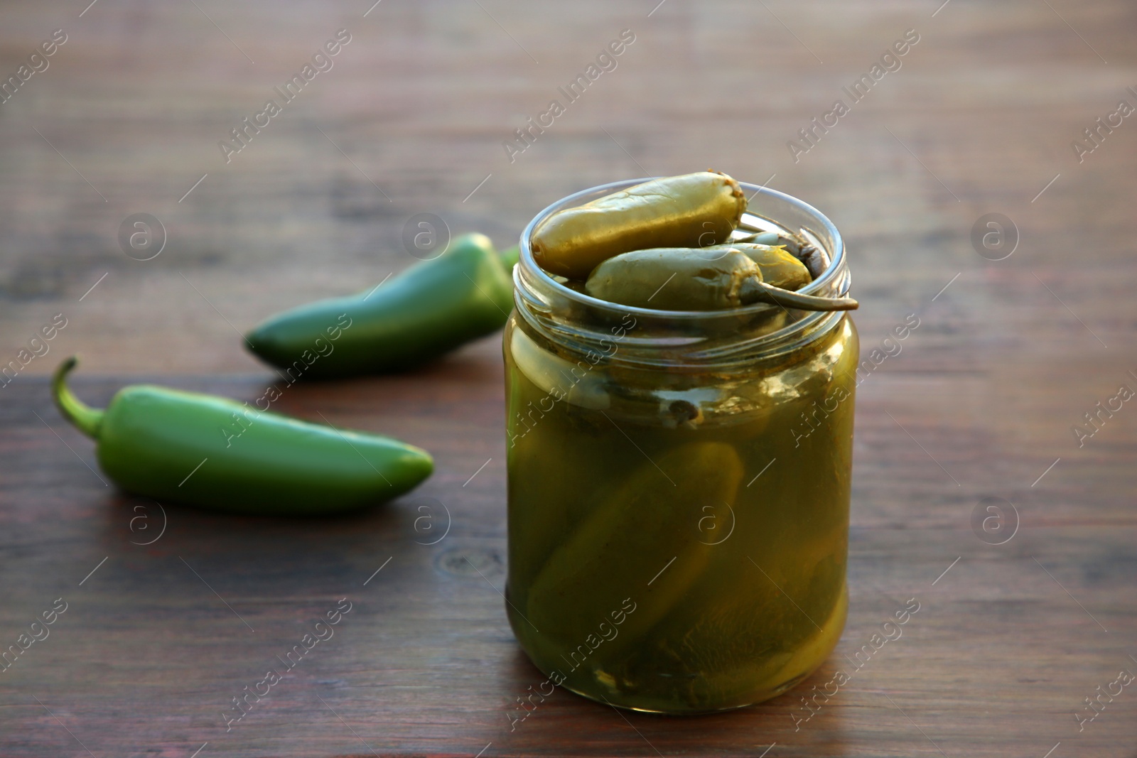 Photo of Fresh and pickled green jalapeno peppers on wooden table