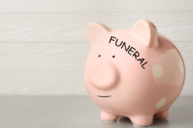 Image of Money for funeral expenses. Pink piggy bank on light grey table. Space for text