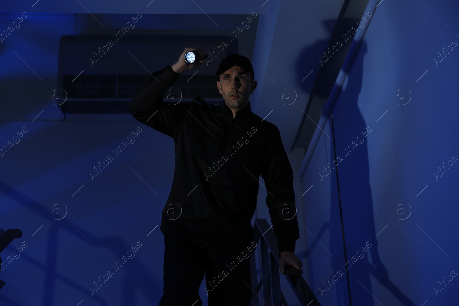 Photo of Male security guard with flashlight on stairs in darkness