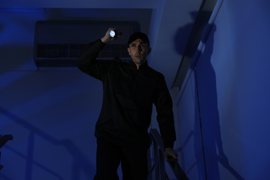 Photo of Male security guard with flashlight on stairs in darkness