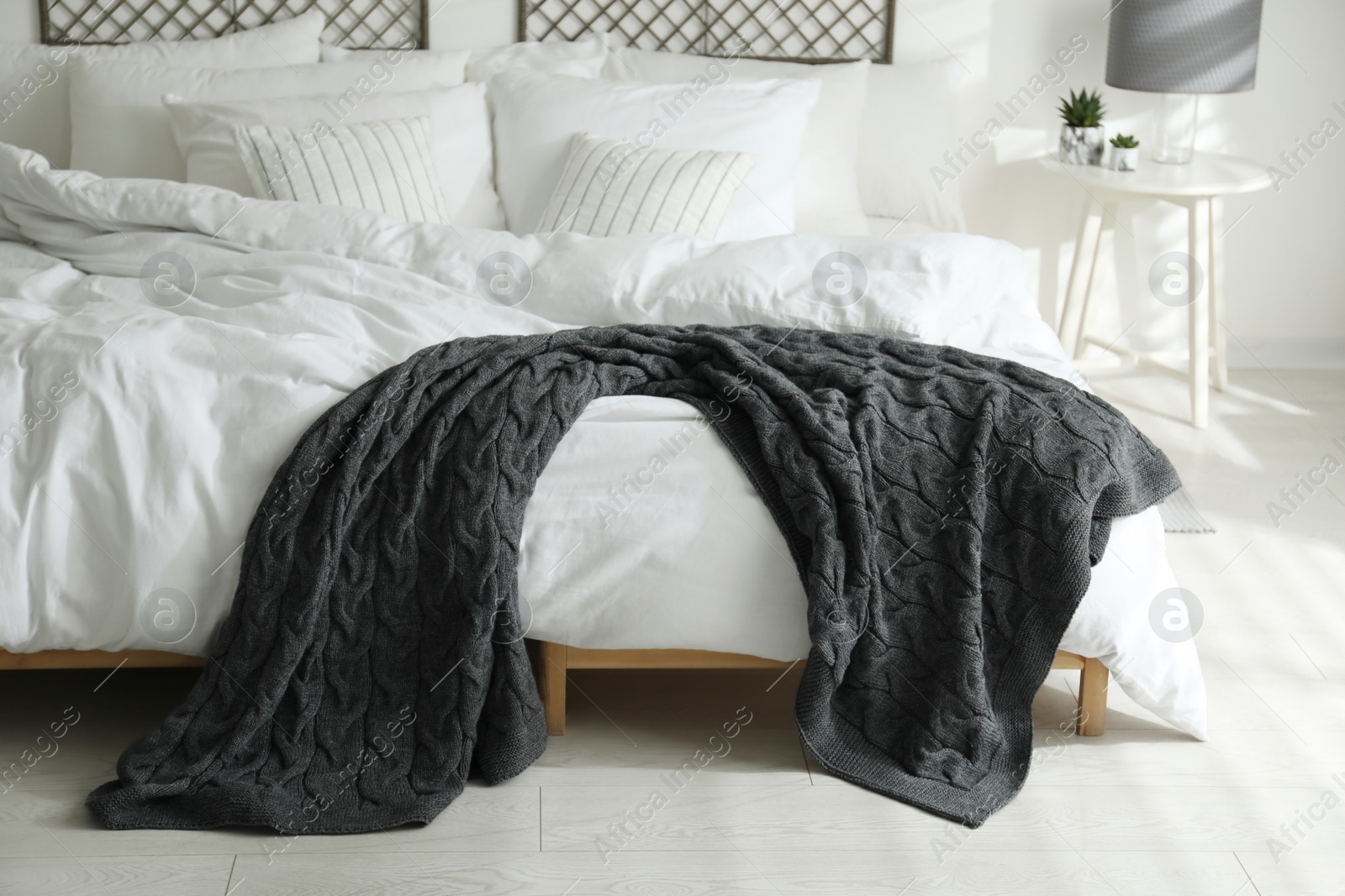 Photo of Comfortable bed with warm knitted plaid in stylish room interior