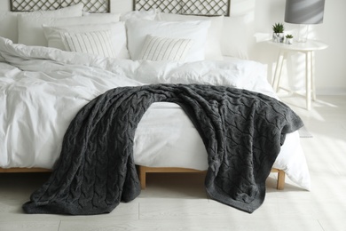 Photo of Comfortable bed with warm knitted plaid in stylish room interior