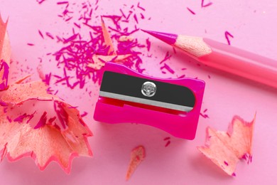 Photo of Pink pencil, sharpener and shavings on light background, flat lay