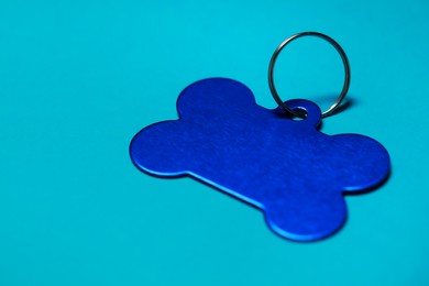 Photo of Pet tag in shape of bone with ring on light blue background, closeup. Space for text