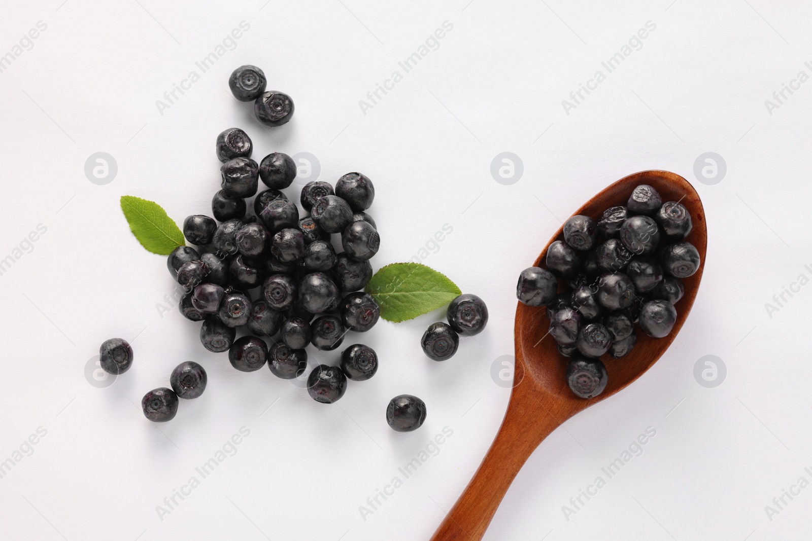 Photo of Spoon with ripe bilberries and leaf on white background, flat lay