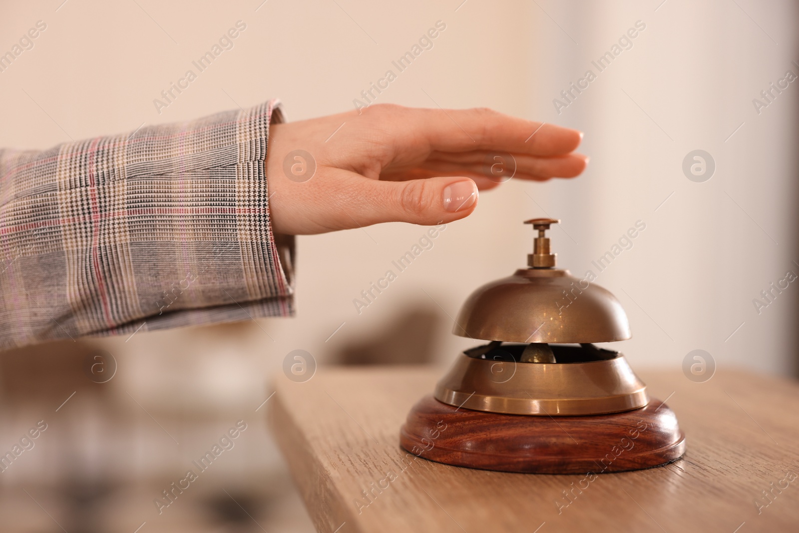 Photo of Woman ringing hotel service bell at wooden reception desk, closeup