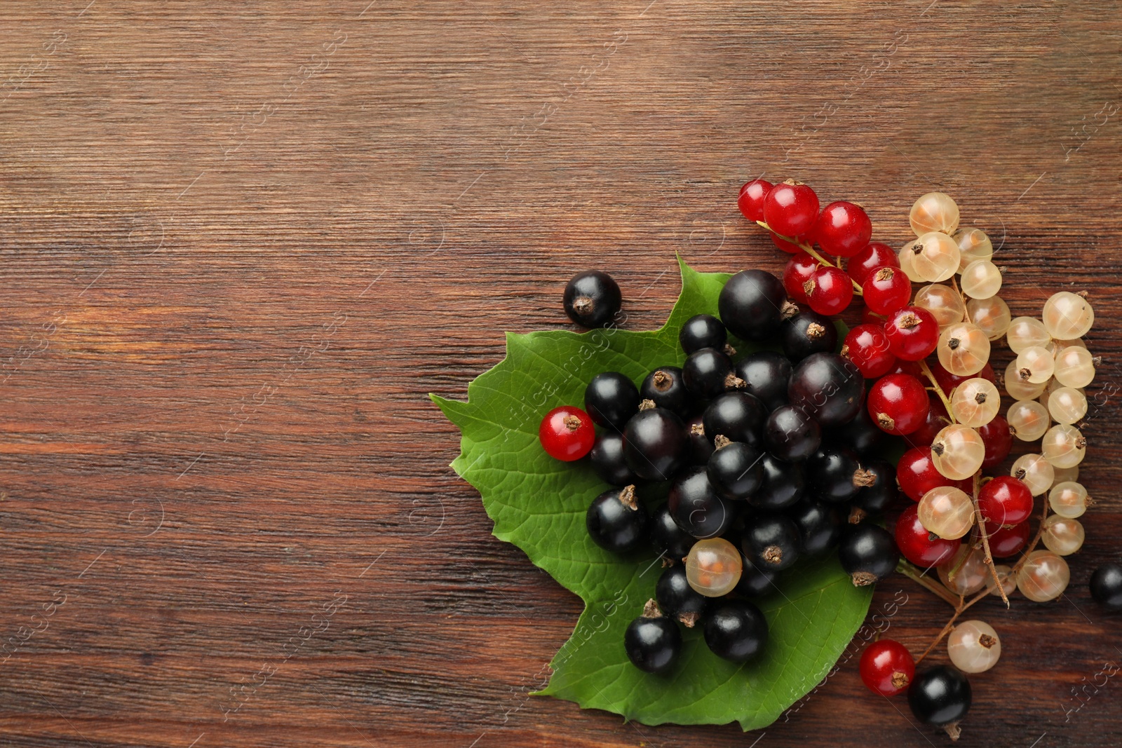 Photo of Different fresh ripe currants and green leaf on wooden table, top view. Space for text