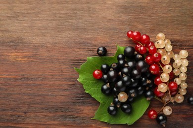 Different fresh ripe currants and green leaf on wooden table, top view. Space for text