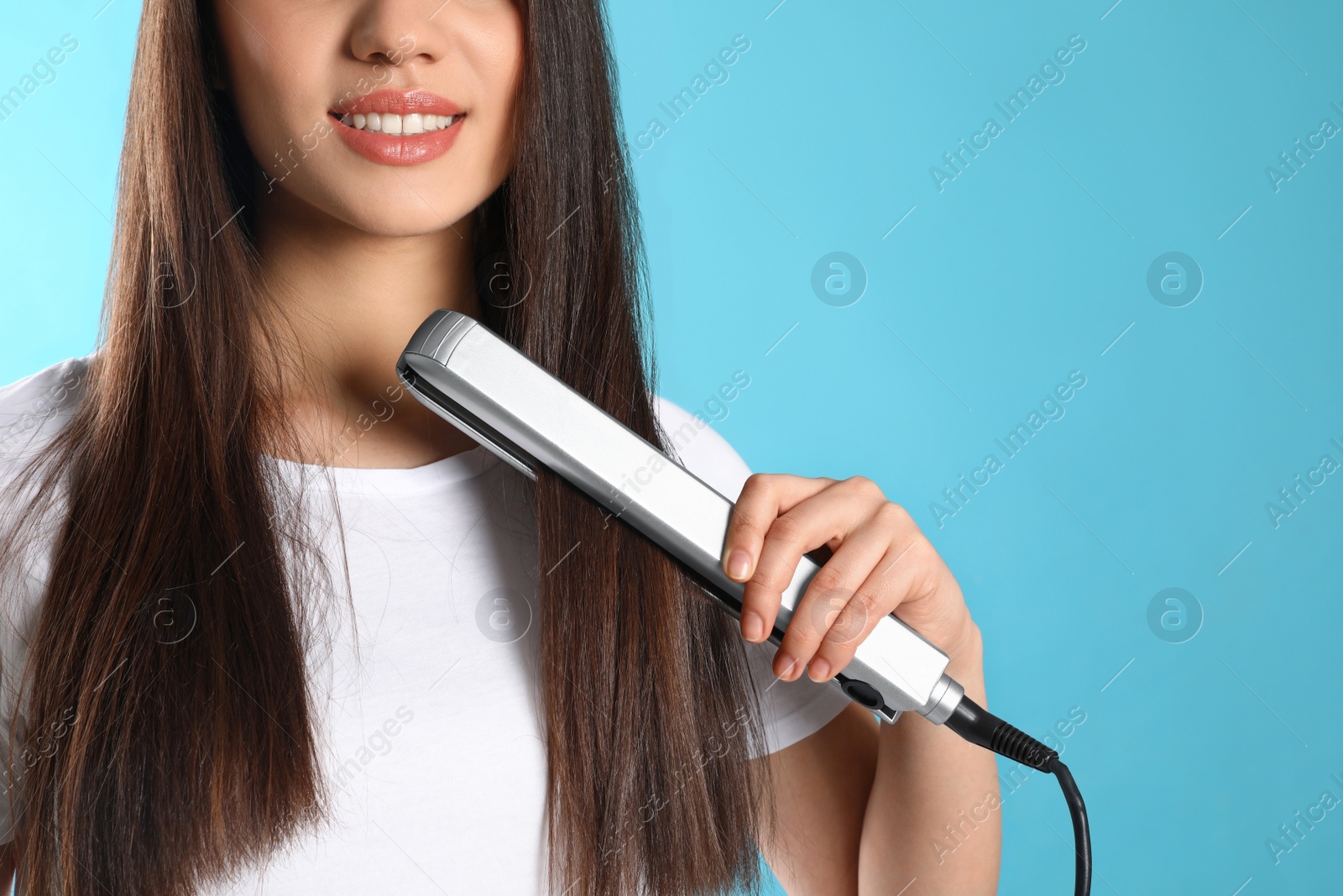 Photo of Happy woman using hair iron on color background, closeup