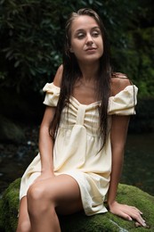 Beautiful young woman in dress sitting on rock near mountain river outdoors