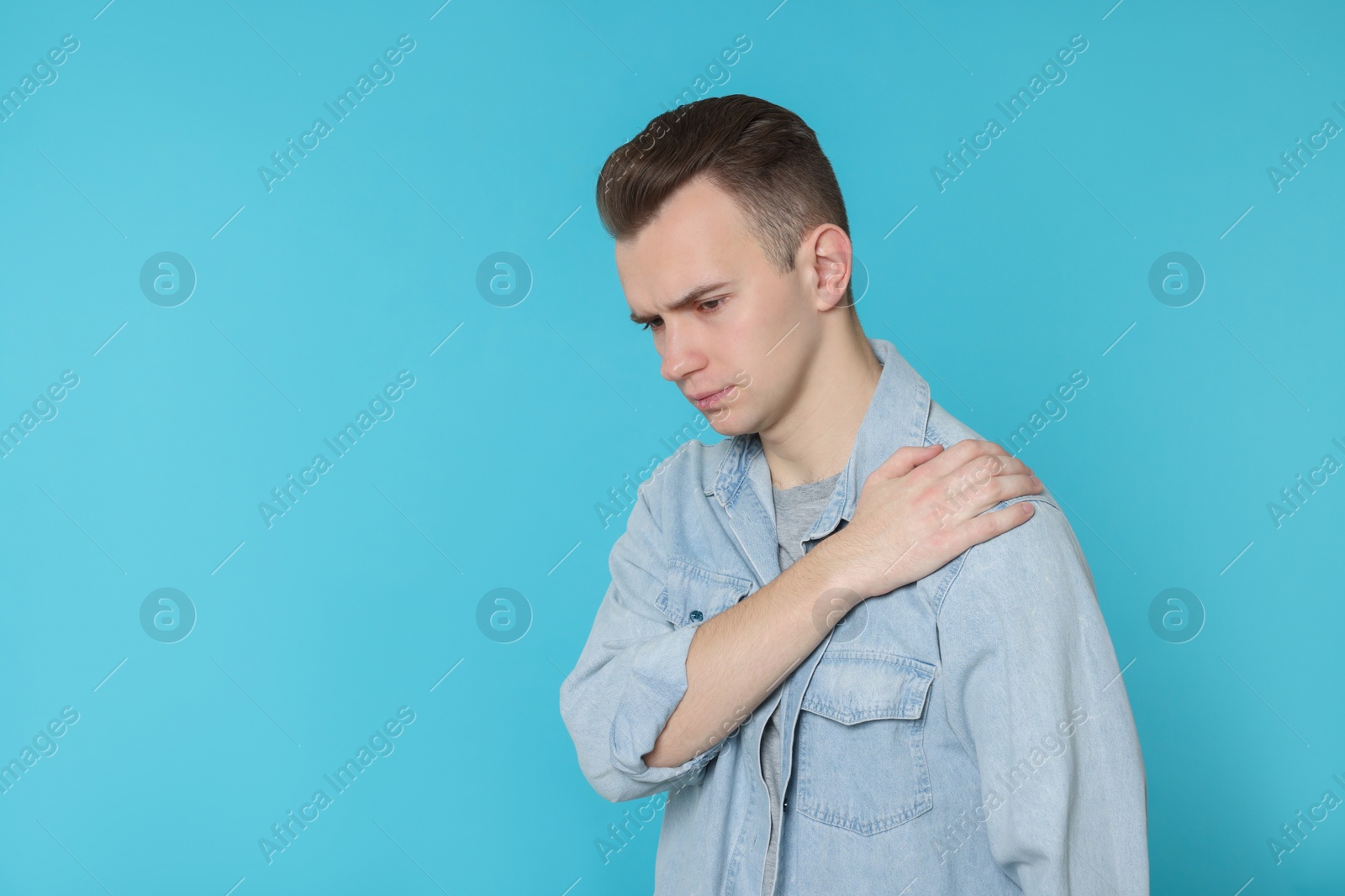 Photo of Young man suffering from pain in his shoulder on light blue background, space for text. Arthritis symptoms