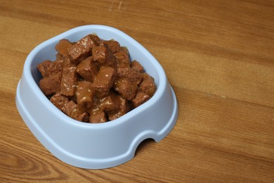 Wet pet food in feeding bowl on wooden background, space for text