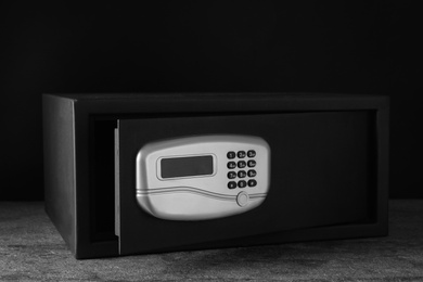 Photo of Black steel safe with electronic lock on grey table against dark background