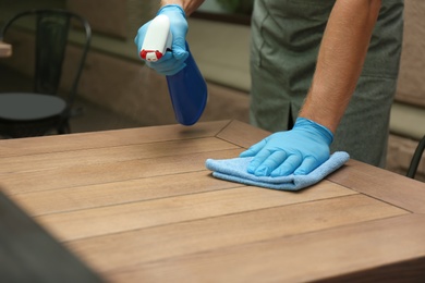 Photo of Waiter in gloves disinfecting table at outdoor cafe, closeup