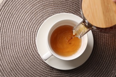 Photo of Pouring aromatic tea into cup at table, top view. Space for text