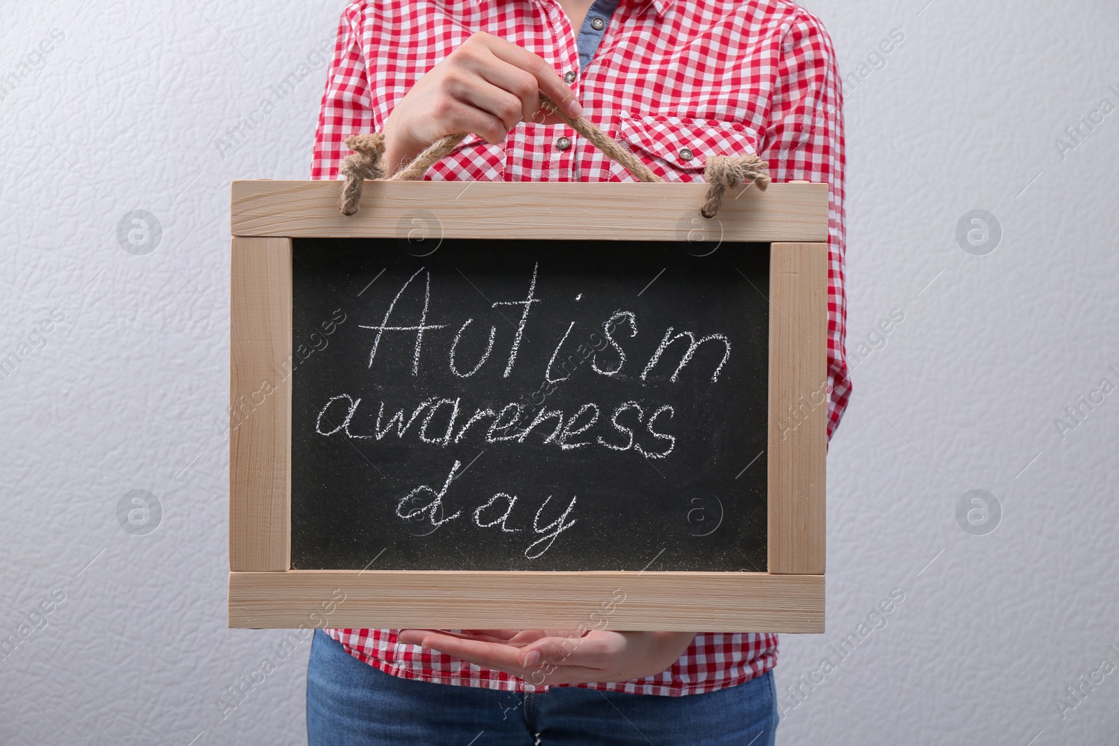 Photo of Woman holding blackboard with phrase "Autism awareness day" on light background