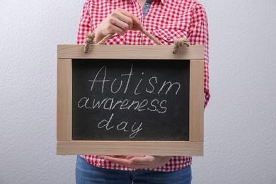 Woman holding blackboard with phrase "Autism awareness day" on light background