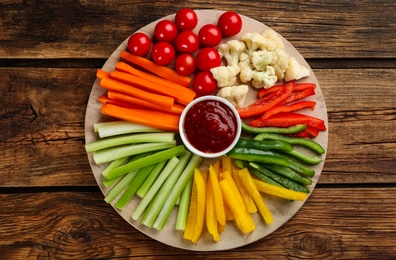 Board with celery sticks, other vegetables and dip sauce on wooden table, top view