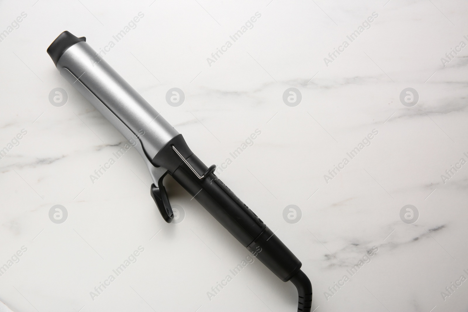 Photo of Hair curling iron on white marble background, top view. Space for text