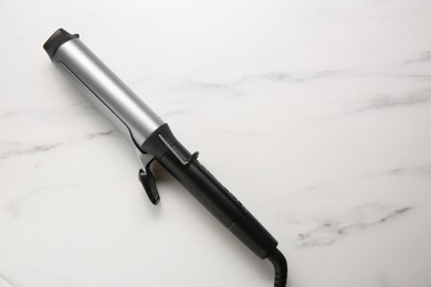 Hair curling iron on white marble background, top view. Space for text