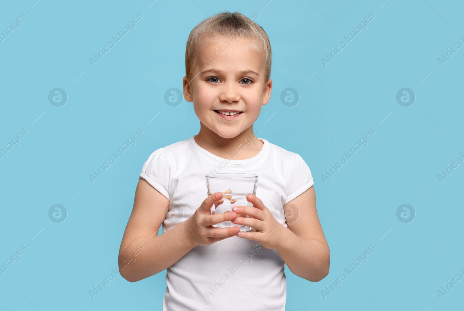 Photo of Happy little girl holding glass of fresh water on light blue background, space for text