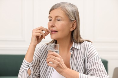 Photo of Menopause, hormone replacement therapy. Woman with glass of water taking pill at home