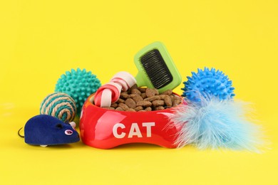 Bowl of dry food, brush and toys on yellow background. Pet shop goods