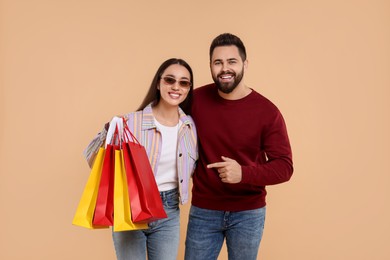 Happy couple with shopping bags on beige background