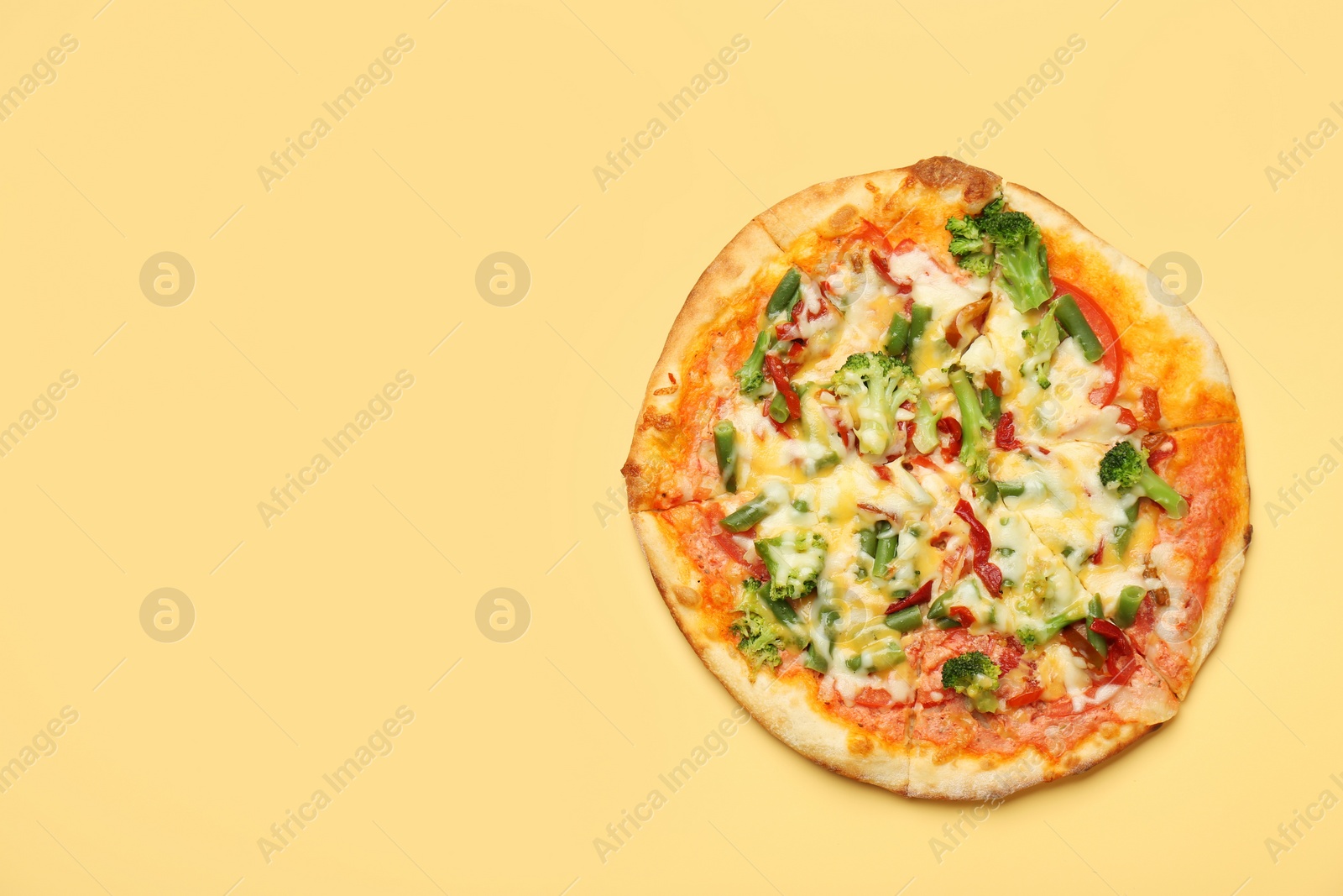 Photo of Delicious vegetarian pizza on yellow table, top view. Space for text