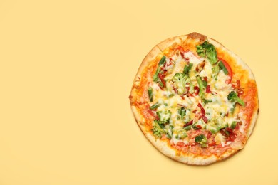 Photo of Delicious vegetarian pizza on yellow table, top view. Space for text