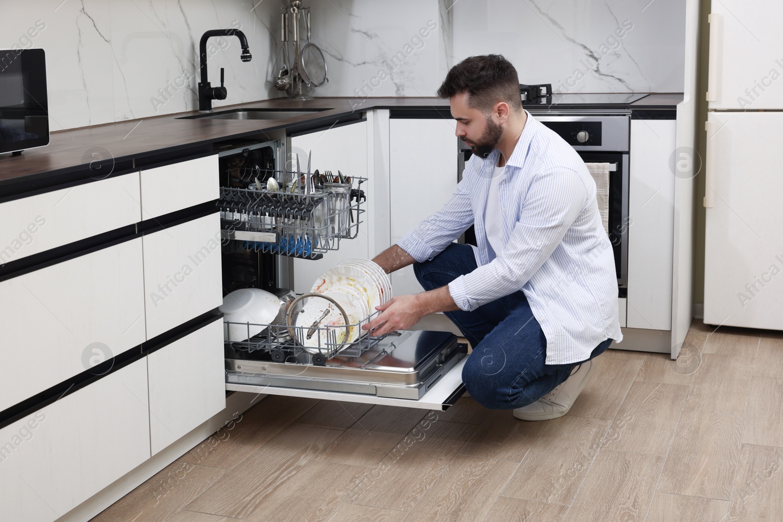 Photo of Man loading dishwasher with dirty plates indoors